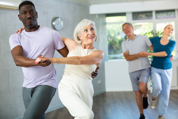 Obraz premium Dynamic mature attendees of dancing courses training Rock and Roll dance poses in dancehall