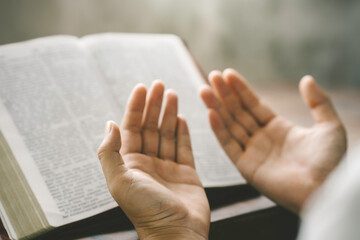Christian hands folded for prayer with a holy bible on a wooden table in church for worship to god...