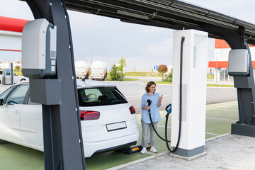 Woman standing near electric car at station