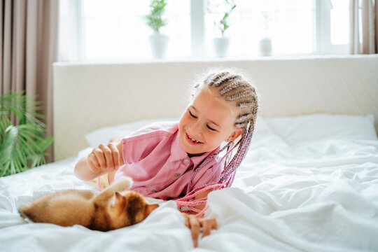 Smiling girl playing with ginger kitten on bed