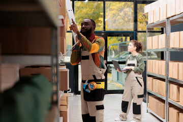 African american worker talking with remote manager at landline phone, discussing goods logistics. Woman supervisor working at customers order, preparing cardboard boxes for shipment in warehouse