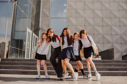 Cheerful schoolgirls dancing in front of school building