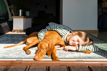 Smiling girl with Vizsla dog relaxing in sunlight at home