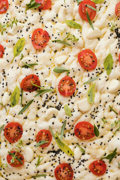 Full frame of focaccia bread dough garnished with tomatioes and black sesame