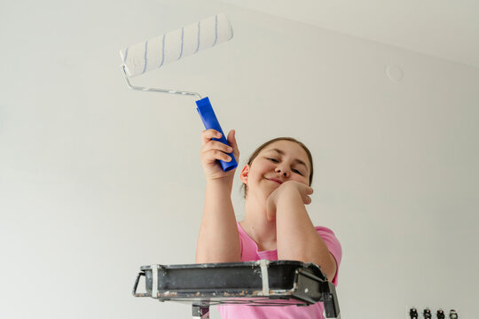 Smiling girl with paint roller in front of wall