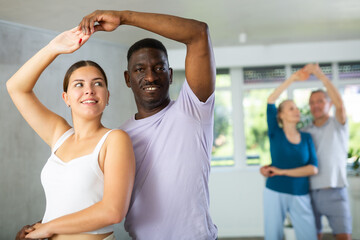 Group of positive young and aged people doing Tango poses in training room during workout session