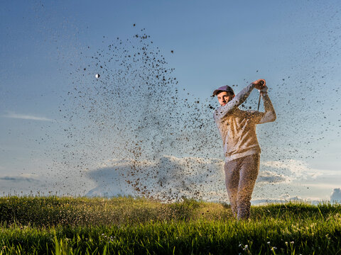 Man playing golf standing on grass at dusk