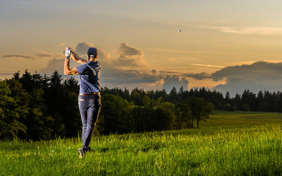 Young man playing golf standing on grass at dusk