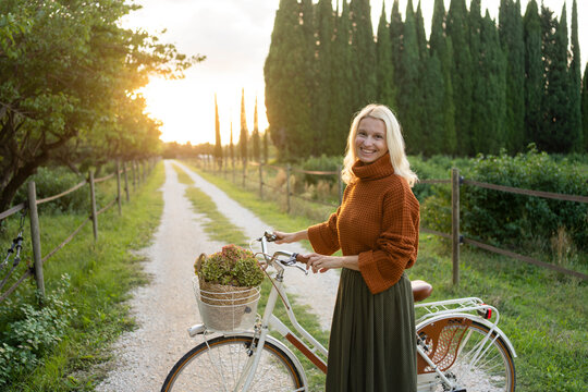Smiling woman standing next to bicycle on footpath