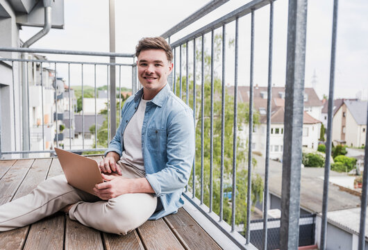 Happy man sitting with laptop on balcony