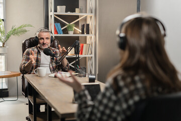 Two radio hosts are sitting in the studio and broadcasting together. Two announcers discuss during a joint broadcast on the radio.