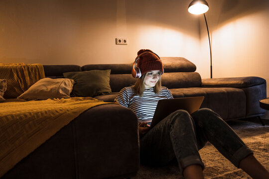 Young woman wearing wireless headphones and using laptop in living room