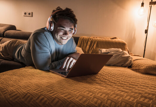 Young Man Wearing Wireless Headphones And Using Laptop In Living Room