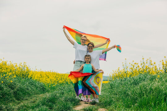 Happy lesbian mothers standing with daughter and holding rainbow flag at field