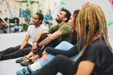 Multi-Cultural Group Watching Friend On Climbing Wall In Indoor Activity Centre