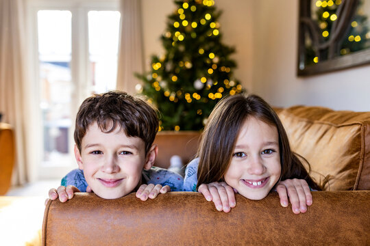 Happy girl with brother having fun on sofa at home at Christmas time