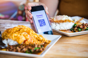 QR code payment tag on smartphone with blurry pork basil stir-fry with fried egg that a spicy Thai dish.