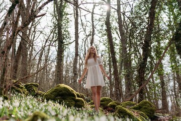 Snowdrops galanthus blonde. A girl in a white dress sits on a meadow with snowdrops in a spring forest