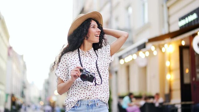 Happy young female tourist in a hat walking along the city street. Lovely lady enjoy the day street lifestyle a girl in hat takes a photo on a camera having good time wandering around town in summer