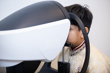 Indian child boy examining eyesight modern ophthalmology equipment  in clinic. Patient kid male scan checkup iris examines ophthalmological hospital.