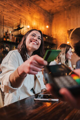 Vertical portrait of happy young woman paying bill with a contactless credit card in a restaurant....