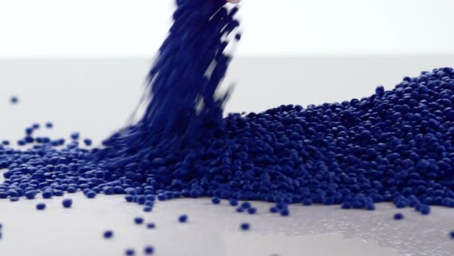 Pile of falling blue plastic grains on a glossy surface with white background