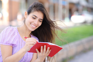 Happy woman writing in red agenda in the street