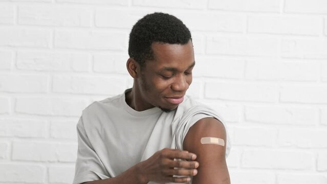 vaccinated African American man showing arm with medical plaster patch Plaster On Shoulder, black male after getting vaccine dose against covid virus, Healthcare immunization, coronavirus vaccination