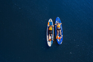Funny man and woman floats on supboard on lake, top view from drone. Concept Summer active sport on water - obrazy, fototapety, plakaty