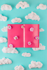 Writer desk concept. Pink open book with clouds. Top view.