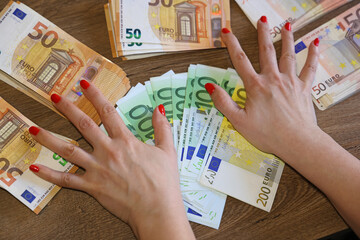 Euro cash money in female hands on the table. Close up of 200, 100 and 50 euro banknotes, concept of good earnings and shopping or business woman
