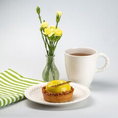 Beautiful elegant white classic porcelain mug with a hot tea drink and pistachio dessert on a porcelain plate served with a mini bouquet of carnations and green striped tea towel. White background.