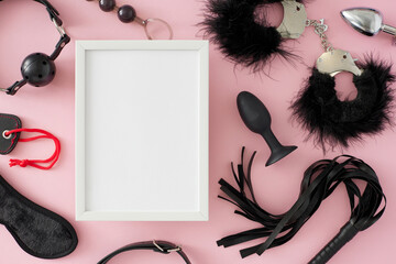 BDSM toy concept for erotic satisfaction. Top view flat lay of black ball gag, fluffy handcuffs, leather whip, anal plugs on pastel pink background with frame for message or promo
