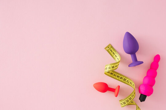 Understanding the role of size in pleasure products theme. Top view flat lay of measuring tape, anal plugs, vaginal plug on pastel pink background with empty space for text or advert