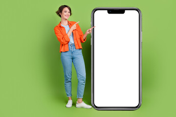 Full length photo of pretty positive lady dressed jeans shirt showing modern gadget empty space isolated green color background
