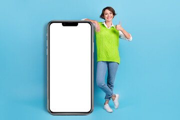 Full length photo of pretty woman with bob hairstyle green waistcoat stand near smart phone thumb up isolated on blue color background
