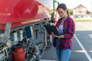 Truck driver holding a laptop and checking the fuel level in the tank, security checks for the safe...