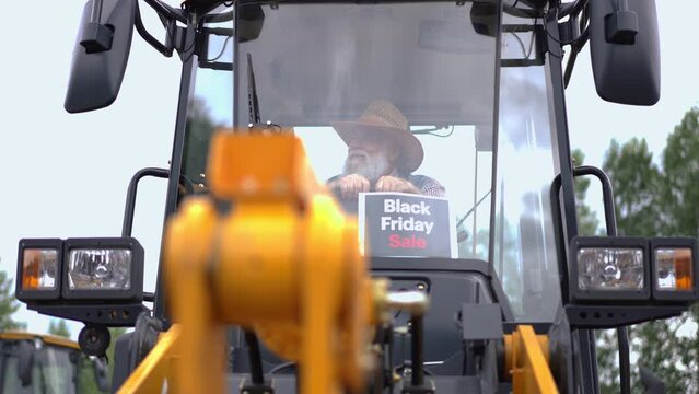 Satisfied senior man sitting in cabin of harvester with Black Friday Sale announcement. Happy confident expert Caucasian farmer buying new machinery for harvesting. Slow motion