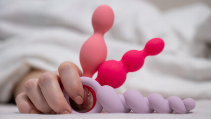 Woman holding three different anal beads while lying in bed. 