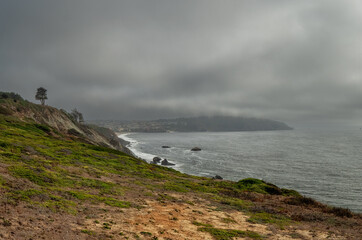 Obraz premium San Francisco Fort Point Rock during a rain shower and a light coming out of the clouds