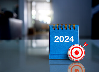 Happy new year 2024 background. 3d target icon on blue small desk calendar standing with 2024 year numbers on glass table at office workplace with copy space. Business goals and success concepts.
