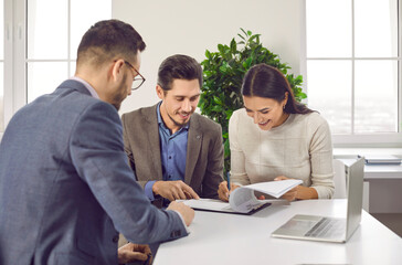 Happy family couple signing paper contract with professional realtor. Satisfied clients making deal...