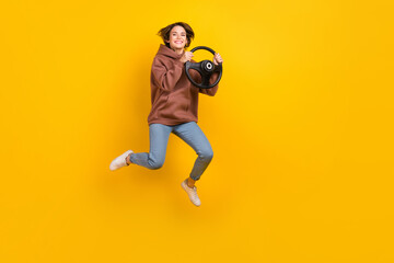 Fototapeta na wymiar Full size portrait of excited girl jumping hands hold wheel empty space isolated on yellow color background