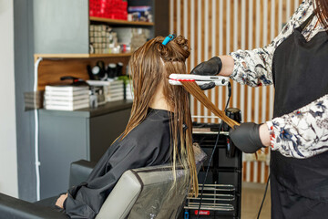 Professional hairdresser straightening long hair using straightener. Hair keratin.