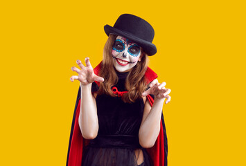 Halloween and childhood. Funny preteen girl playfully scares you by attacking and scratching during Halloween fun. Creative smiling child in Halloween costume makes claw gesture on orange background.