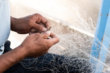 The man is repairing a fishing net on a boat in a village, Indonesia - Powered by Adobe