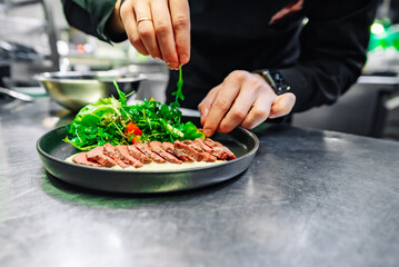 chef hand cooking Roast beef salad with vegetables on restaurant kitchen