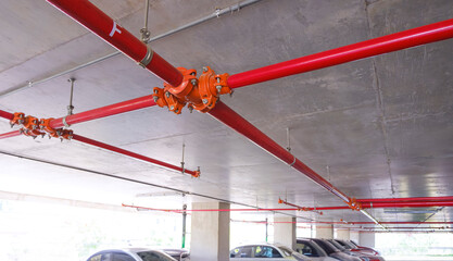 Red fire protective water pipeline system on concrete ceiling inside of parking garage building,...