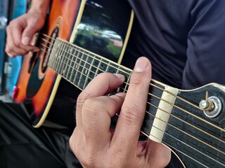 Asian man playing guitar holding G chord and F chord in garden.