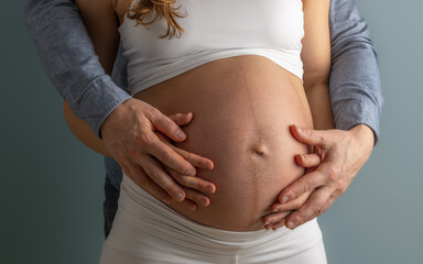 Mid-section of mother and father holding naked round pregnant belly with thier hands in last month...